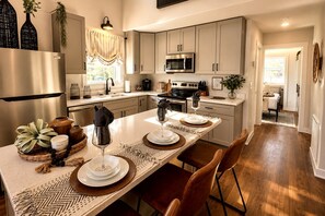 A modern kitchen with a central island, stainless steel appliances, and a dining area with a table set for two. - Lofted Tiny Retreat with Private Lake Dock and Spa in Tennessee (Tracy City)