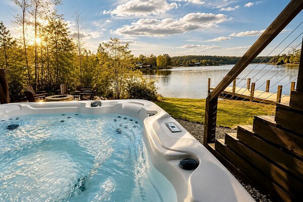 Un bain à remous avec vue sur un lac et des arbres, entouré d’une terrasse en bois et de chaises.