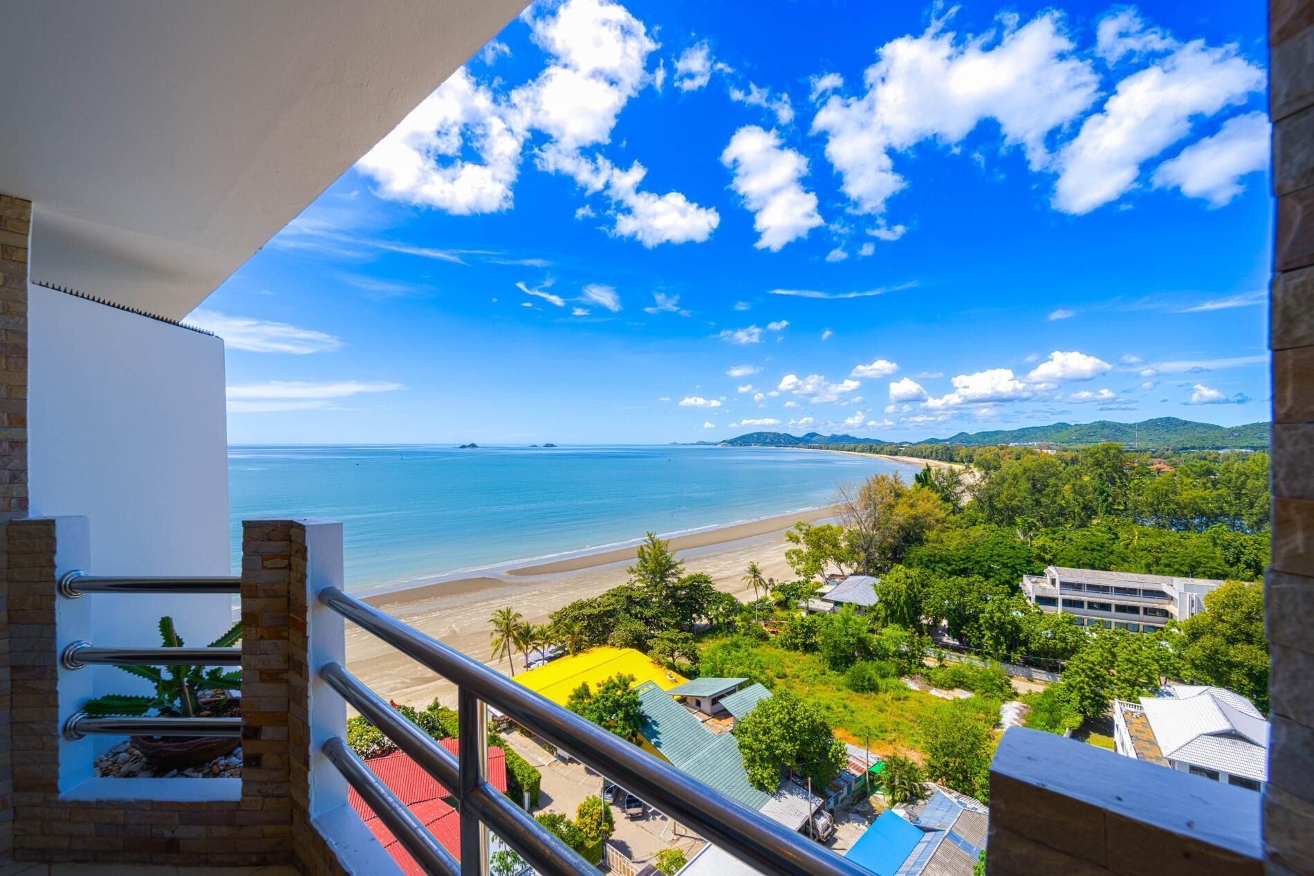 Un balcone con vista sulla spiaggia, l'oceano e il verde circostante.