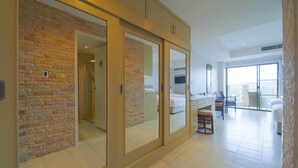 A modern hotel room with a brick wall, a large sliding door, a balcony with a view, and a spacious living area. - Beachfront Studio Condo-Seaview BW1 (Hua Hin)