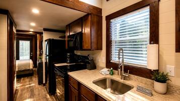 Cocina compacta con armarios de madera, refrigerador negro, estufa y pileta.