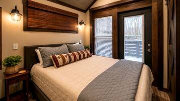 A bedroom with a bed, bedside tables, a wall-mounted light fixture, and a door with a view of the outside.