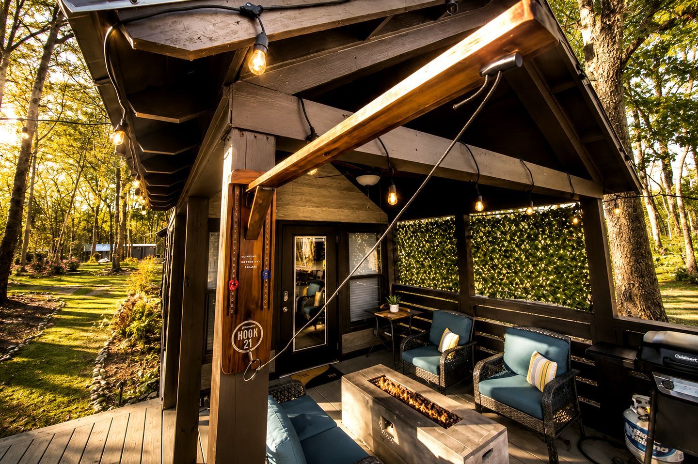 A covered outdoor seating area with a fire feature, wooden deck, and a view of the surrounding trees.