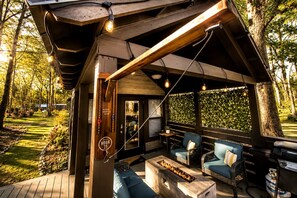 A covered outdoor seating area with a fire feature, wooden deck, and a view of the surrounding trees. - Gorgeous Cabin with Hot-tub and Games in Monteagle, Tennessee (Monteagle)