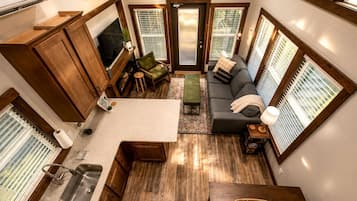 Un espacio habitable pequeño con kitchenette, zona de estar y ventanas amplias.