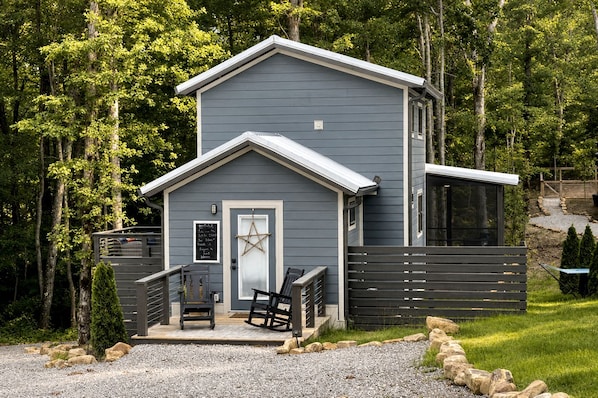 A two-story cabin with a front porch, a wooden fence, and a gravel driveway.