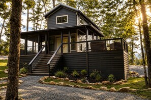 Una cabana de dues plantes amb un porxo cobert, una escala i vistes a la forest circumdant.