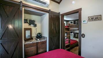 A bedroom with a bed, a dresser, an air conditioning unit, and a door leading to a cabin area.