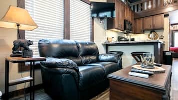 A living room with a black leather sofa, a wooden coffee table, a lamp, and a kitchen area in the background.