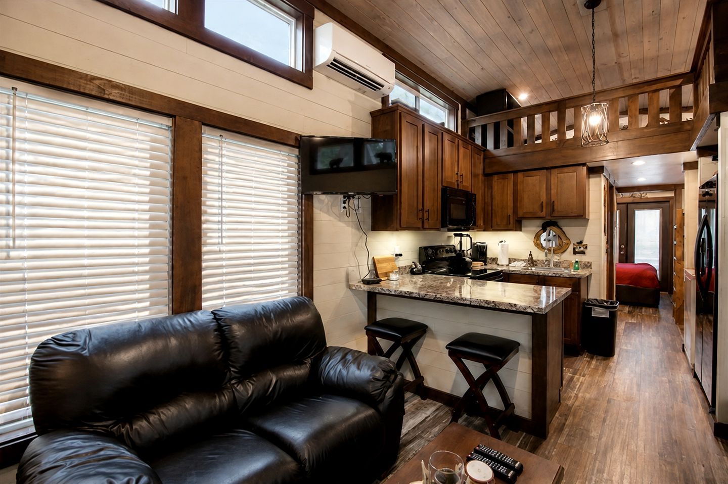 A compact kitchen with a central island, wooden cabinets, and a black leather sofa in a living area.