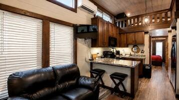 A compact kitchen with a central island, wooden cabinets, and a black leather sofa in a living area.