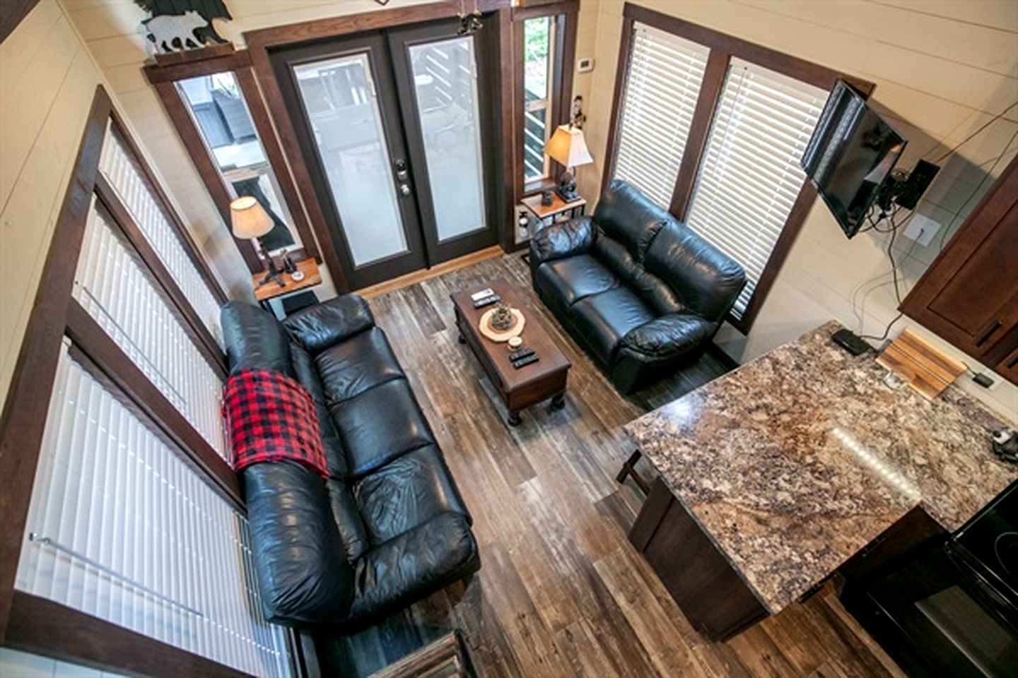 A spacious living area with a black leather sofa, a coffee table, and a kitchen counter with a granite backsplash.