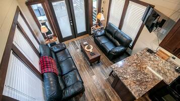 A spacious living area with a black leather sofa, a coffee table, and a kitchen counter with a granite backsplash.