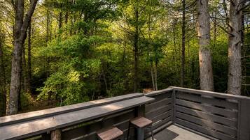 A wooden deck with a railing, two stools, and a bench overlooking a forest.