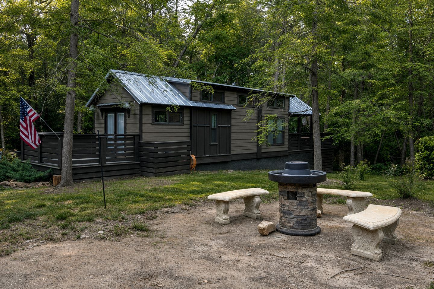 A cabin with a metal roof, surrounded by trees, and a stone fire pit with benches.