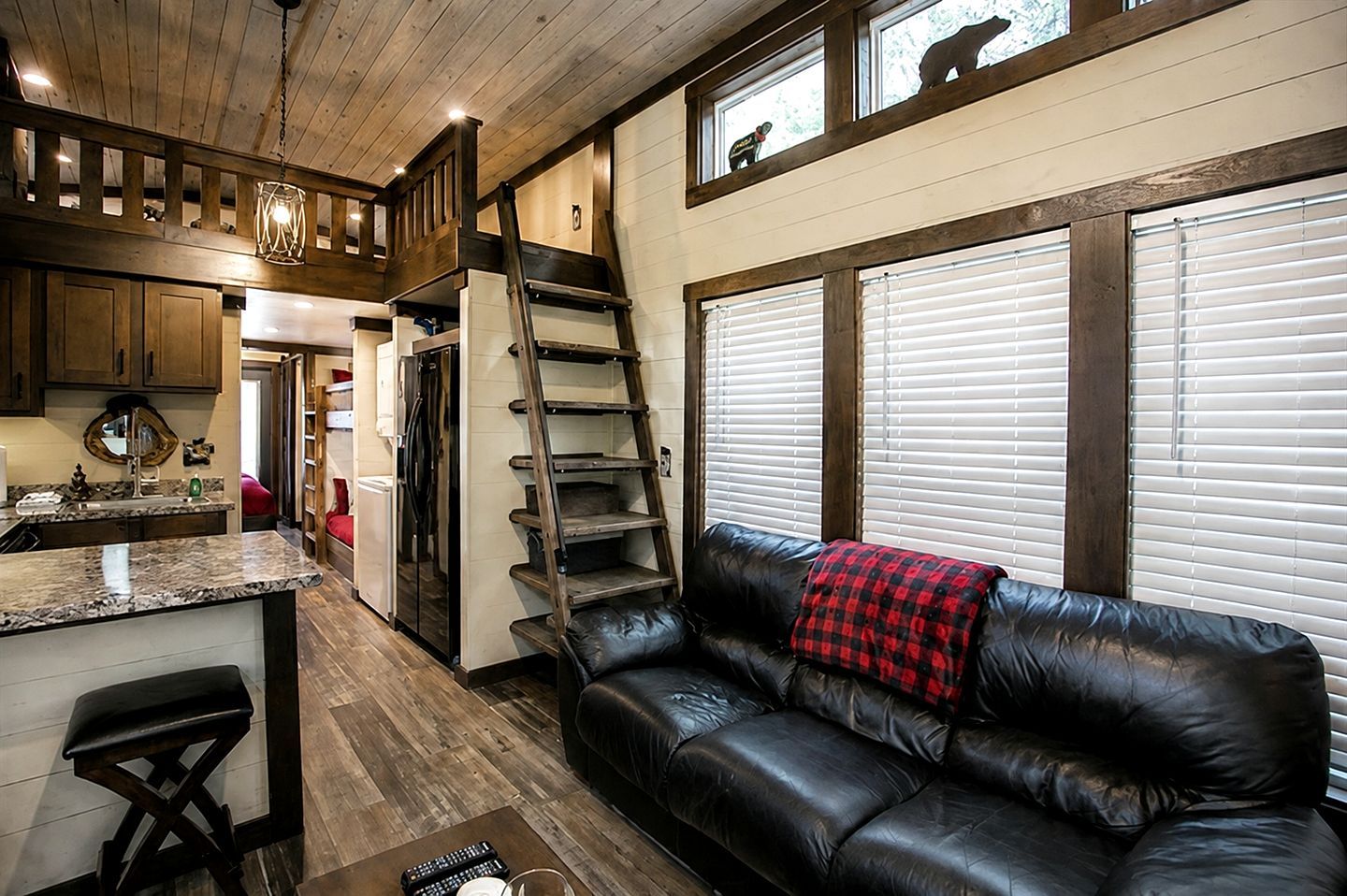 Un intérieur chaleureux avec un plafond en bois, un canapé en cuir noir, un coin cuisine et un espace en mezzanine accessible par une échelle.