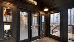 A wooden deck with a welcome mat, a door with frosted glass panels, and a view of a snowy landscape. - Tranquil Cabin with Fire Pit and Panoramic Lake Views in Tennessee (Tracy City)