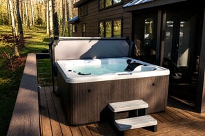 Ein Whirlpool auf einer Holzterrasse mit Stufen, umgeben von einem Holenzaun und einem Haus im Hintergrund.
