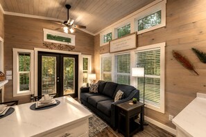 A cozy living room with a dark gray sofa, a ceiling fan, and a dining area with a white table. - Tranquil Cabin with Fire Pit and Panoramic Lake Views in Tennessee (Tracy City)