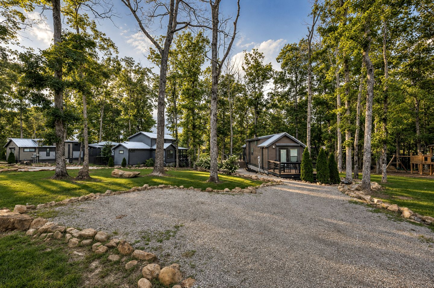 A campground with multiple cabins, a gravel driveway, and surrounding trees.