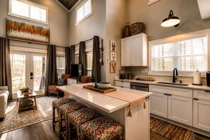 A modern kitchen with a central island, white cabinetry, and a large window providing natural light.