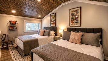 A bedroom with two beds, a window, a wooden ceiling, and wall art.