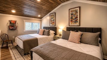A bedroom with two beds, a window, a wooden ceiling, and wall art.