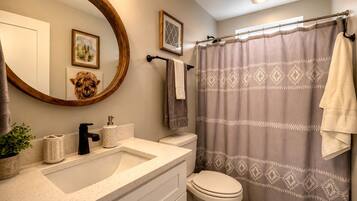 A bathroom with a round mirror, a sink with a soap dispenser, a toilet, and a shower curtain with a geometric pattern.