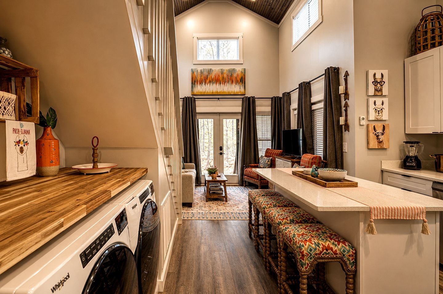 A compact kitchen with a built-in washer and dryer, a dining area with a bench, and a living space with a sofa and TV.