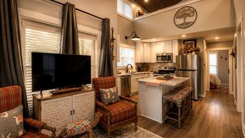 Una cocina moderna con una televisión de pantalla plana, una zona de comedor con un sofá rojo a cuadros y una mecedora de madera.