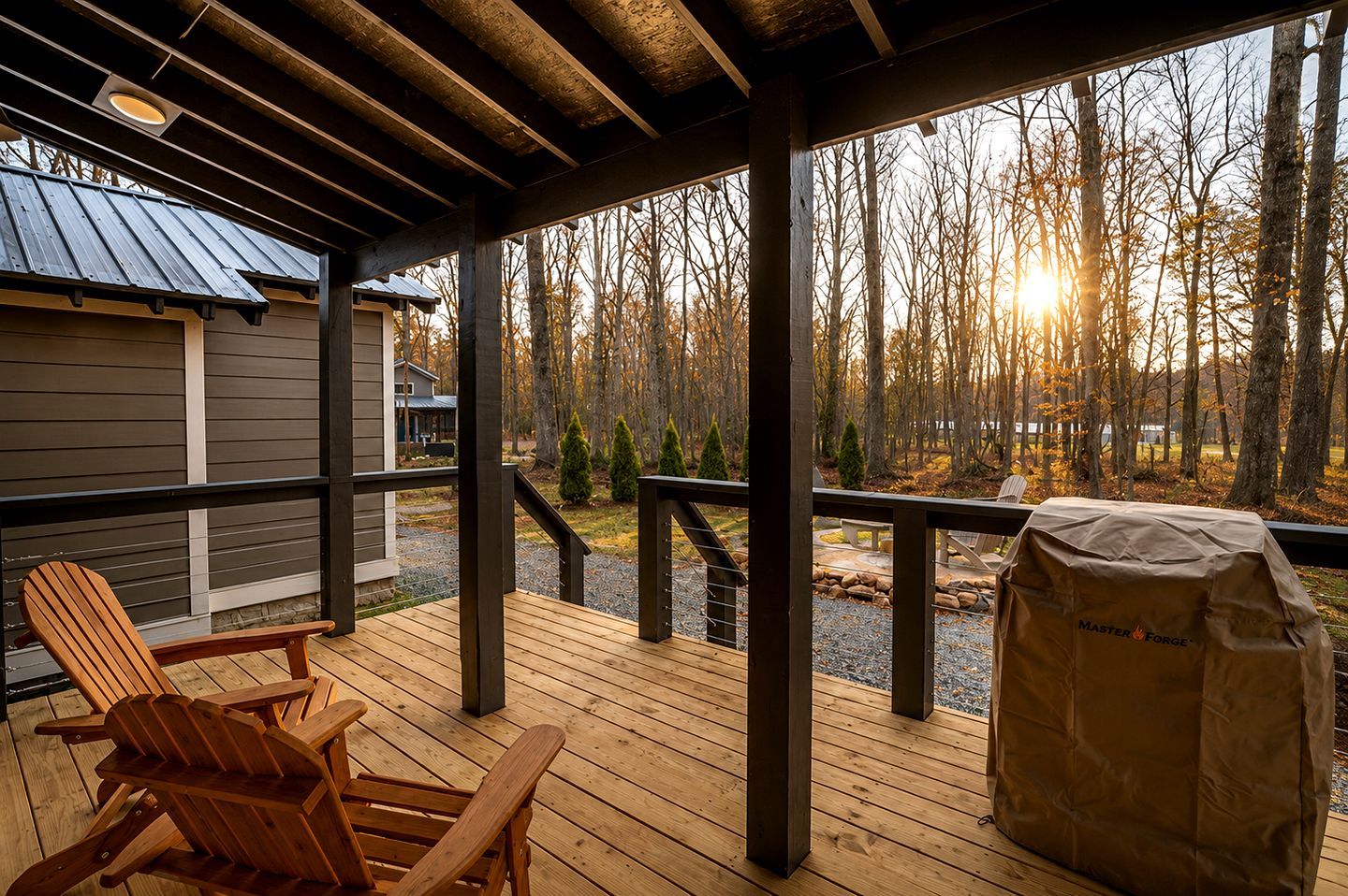 Una terraza de madera con sillas Adirondack, una parrilla y vista a un bosque.