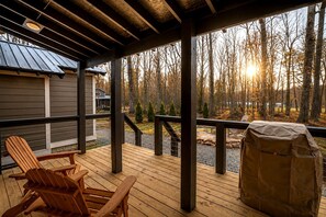 A wooden deck with Adirondack chairs, a barbecue grill, and a view of a forest. - Incredible Cabin with Fire Pit and Great Vistas in Monteagle, Tennessee (Monteagle)