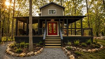 A cabin with a red door, wooden deck, and a covered porch.
