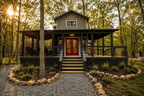 A cabin with a red door, wooden deck, and a covered porch.