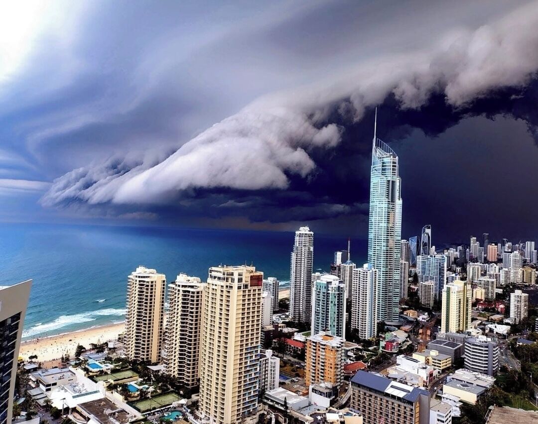A coastal cityscape with high-rise buildings, a beach, and a stormy sky.