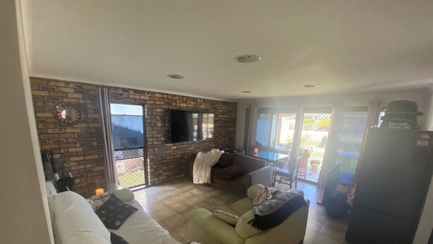 A living room with a brick wall, a flat-screen TV, a sofa, and a refrigerator. - Room-exclusive Sunrise Room, GC Blues Fe (Gold Coast)