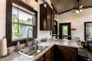 A kitchen with a granite countertop, stainless steel sink, wooden cabinets, and a ceiling fan. - Breathtaking Cottage with Fire Pit in Tracy City, Tennessee (Tracy City)