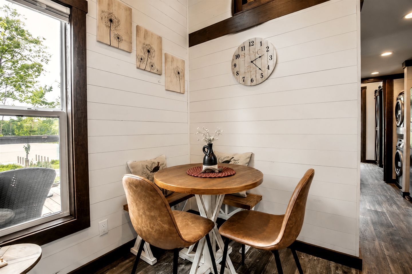 Un comedor con una mesa redonda, cuatro sillas, un reloj y una obra de arte colgada en la pared.