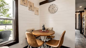 Un comedor con una mesa redonda, cuatro sillas, un reloj y una obra de arte colgada en la pared.