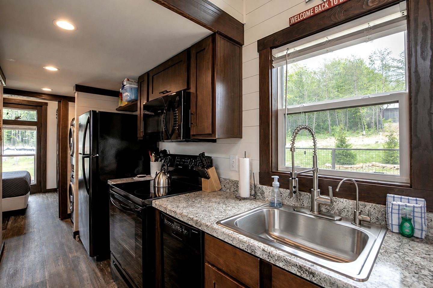 Una cocina moderna con armarios de madera oscura, electrodomésticos de acero inoxidable, encimera de granito y ventana con vistas a zonas verdes.