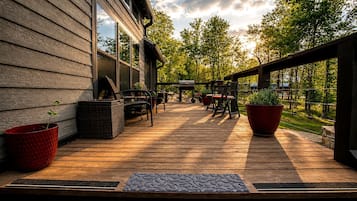 Una terraza de madera con mobiliario exterior, una parrilla y macetas con plantas.