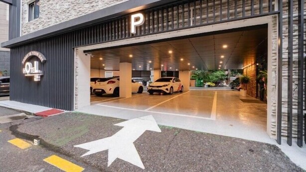 A hotel parking garage with a 'P' sign above the entrance, a covered area with cars parked inside, and a directional arrow on the ground. - Hotel Oneul (Incheon)