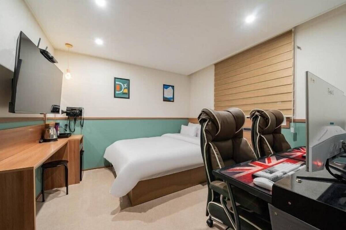 A hotel room with a bed, a desk with a computer, a TV, and a massage chair.