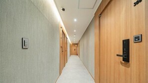 A hallway with wooden doors, a carpeted floor, and a light switch on the wall. - Hotel Oneul (Incheon)