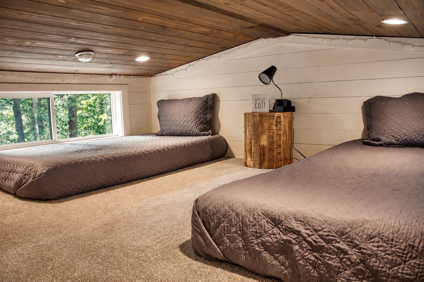 Een slaapkamer met twee bedden, een nachtkastje met een lamp en een raam met uitzicht op bomen.