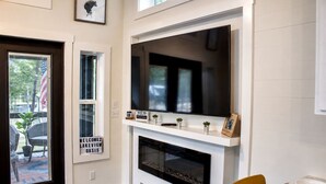 Una sala de estar moderna con chimenea, un televisor montado encima y un cartel dando la bienvenida a los huéspedes en Oasis.