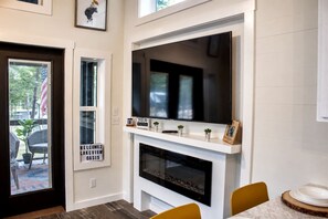Ein modernes Wohnzimmer mit Kamin, einem darüber montierten Fernseher und einem Schild, das Gäste zum Oasis willkommen heißt.