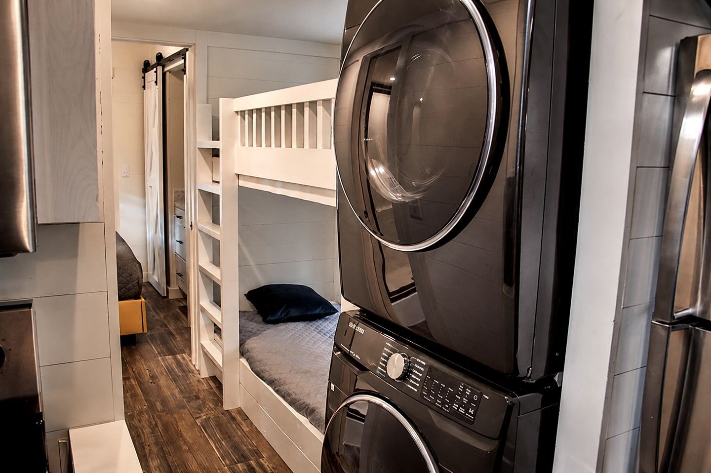 A compact laundry room with a washing machine, a dryer, and a bunk bed with a mattress and pillow.