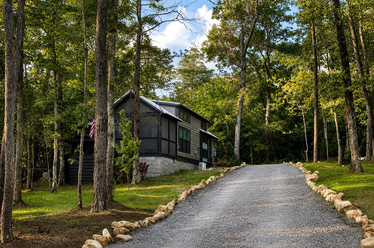 A cabin with a gravel driveway surrounded by trees.