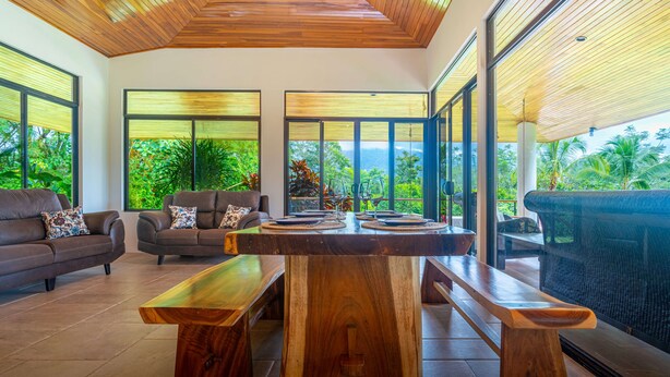 Un salón amplio con una mesa de centro de madera, sofás de cuero y ventanas grandes que ofrecen vistas a vegetación exuberante.